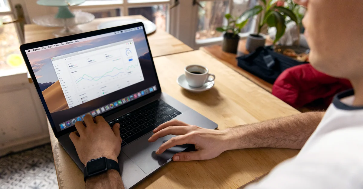 Une personne travaillant sur un ordinateur portable avec des analyses commerciales affichées, montrant une configuration de télétravail dans un environnement confortable.