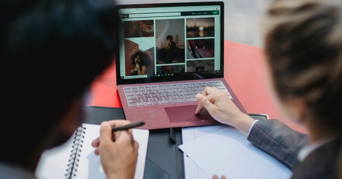 Deux professionnels travaillant sur un ordinateur portable à une table, discutant du contenu et prenant des notes.