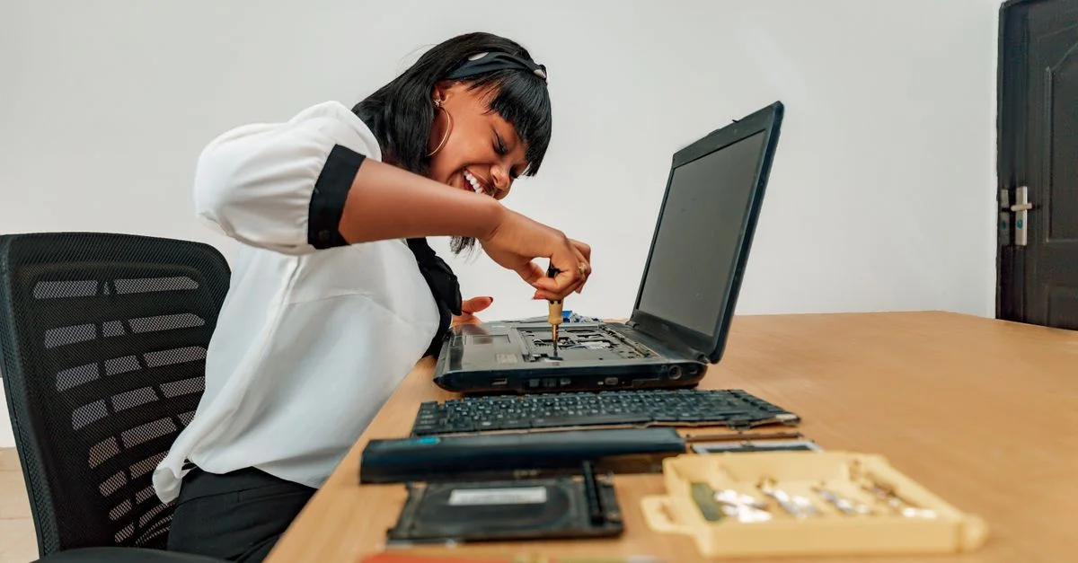 Femme réparant un ordinateur portable à un bureau avec des outils, mettant en avant la technologie et l'habileté.