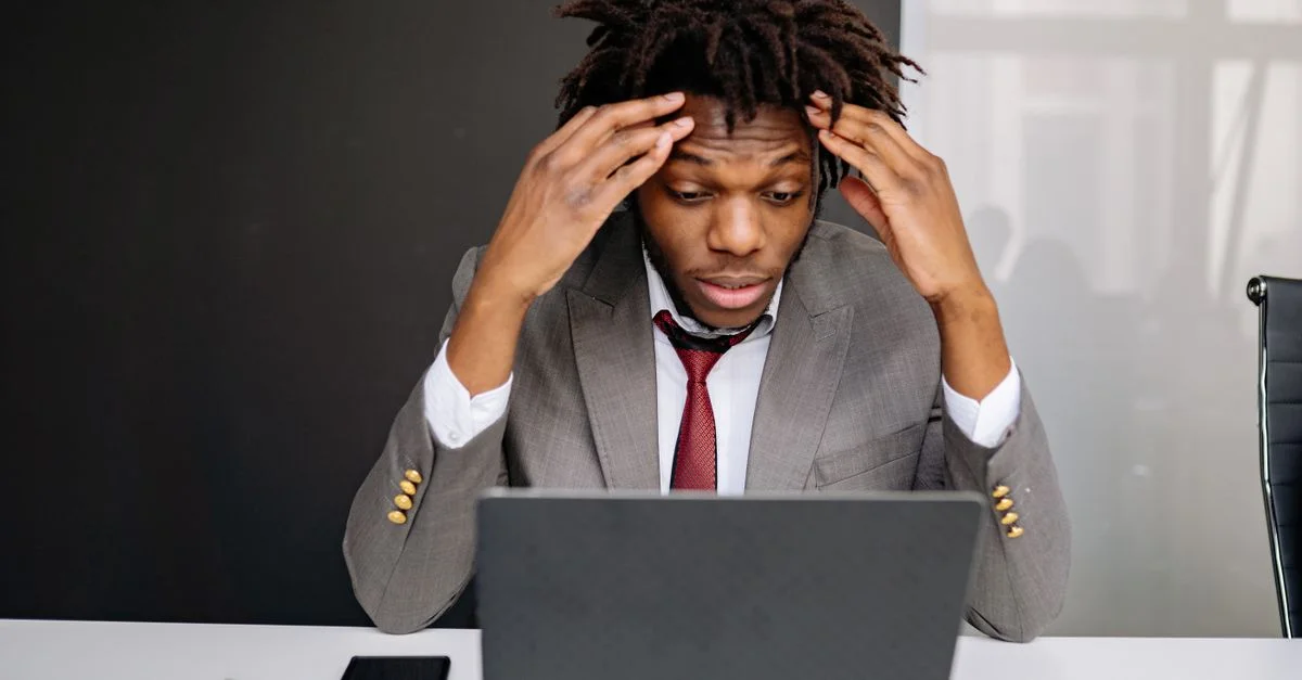Homme d'affaires afro-américain ressentant du stress en travaillant sur un ordinateur portable à l'intérieur.