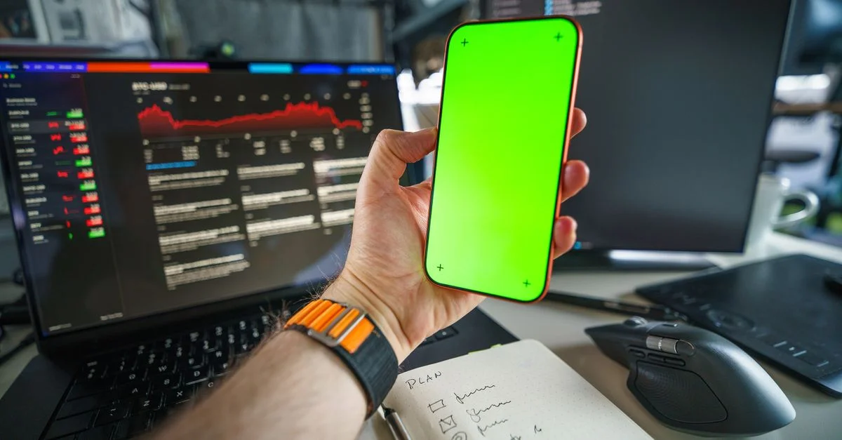 Espace de travail moderne avec un smartphone à fond vert, un ordinateur portable avec des données financières et des gadgets technologiques.