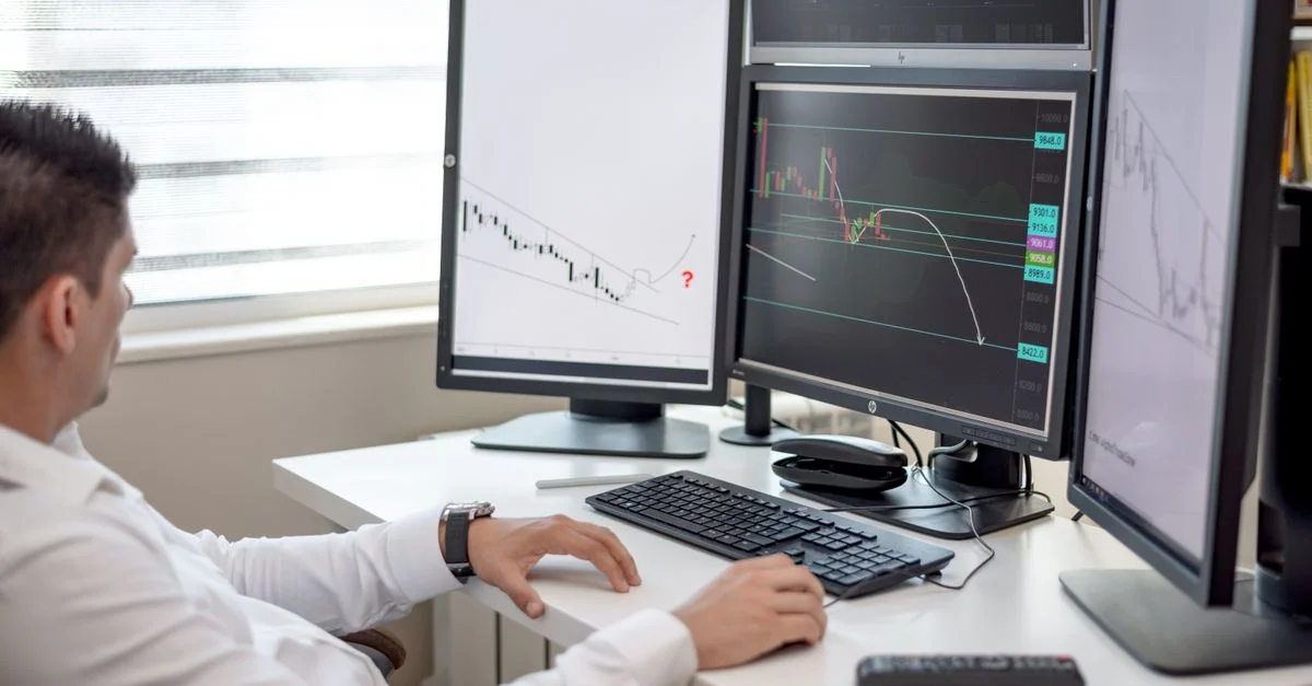 Un homme d'affaires à son bureau analysant des graphiques financiers sur plusieurs écrans.