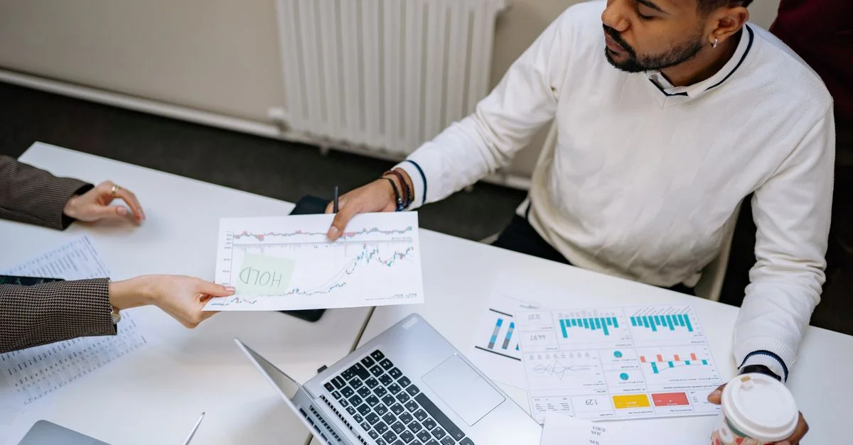 Des collègues collaborant sur des graphiques financiers et des données lors d'une réunion d'affaires à l'intérieur.