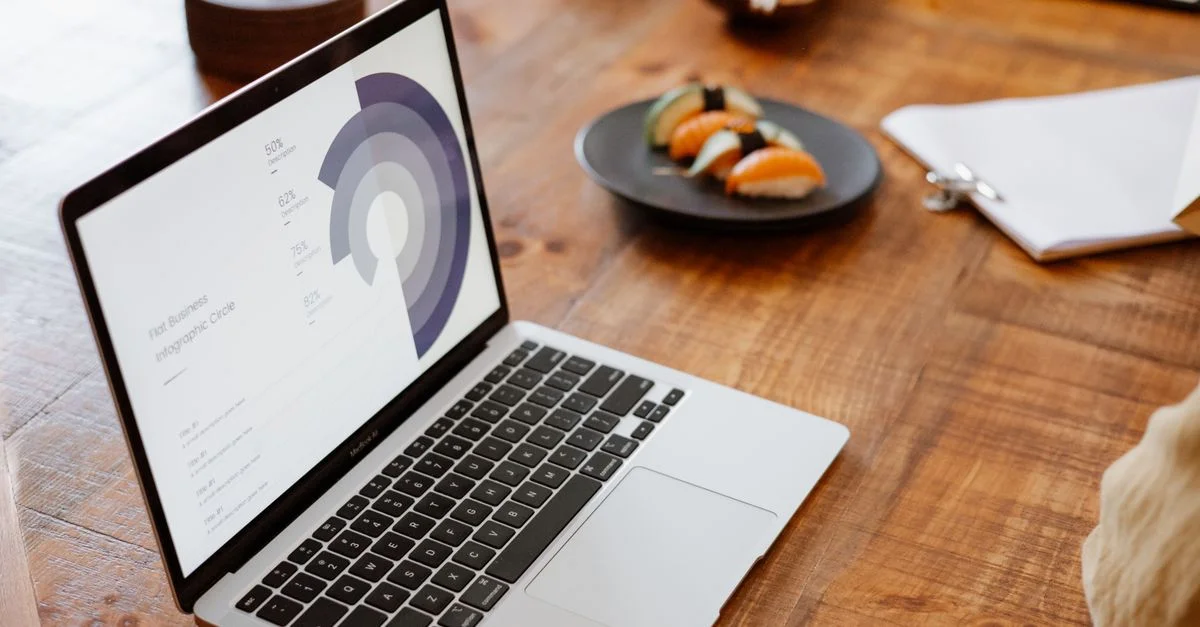 Ordinateur portable affichant des données sur une table en bois avec une assiette de sushi, idéal pour des thèmes de style de vie ou d'affaires.