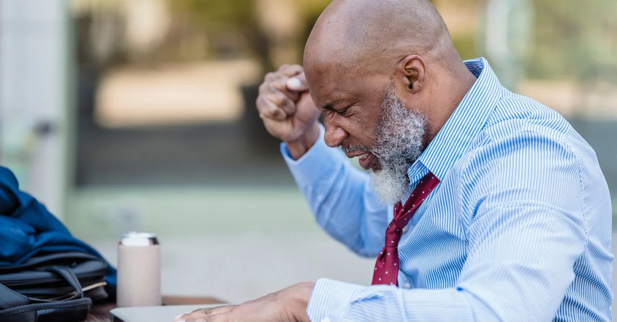 Un homme chauve avec une barbe regardant frustré son ordinateur portable en étant assis à l'extérieur.